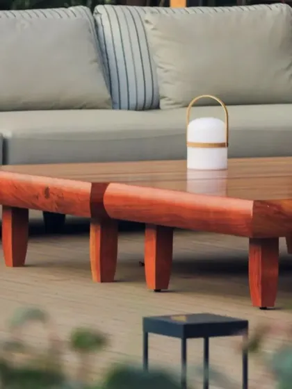 A close-up of the custom outdoor coffee table, crafted from a solid piece of wood. The furniture is both durable and sculptural, adding to the earthy, minimalist setting.