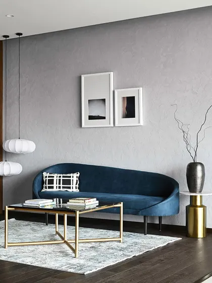 The deep blue velvet sofa is a focal point, adding a touch of color and luxury against the neutral grey wall and dark wood floors.