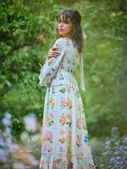 A shot from a creative campaign for Pozruh, set in a lush, floral environment. The styling of this printed maxi dress is soft and romantic, perfectly matching the "secret garden" theme.