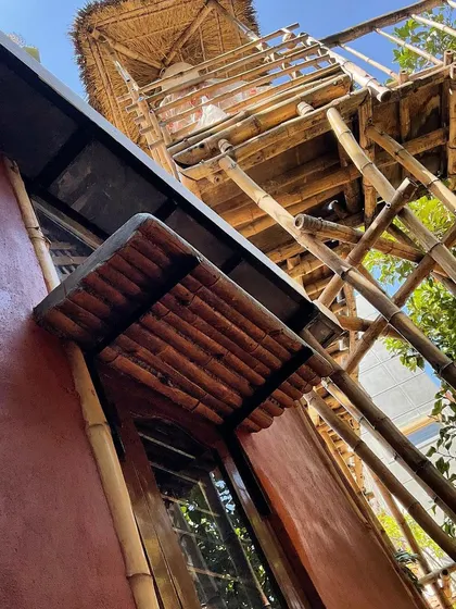 This cottage exterior features bamboo chajjas (eaves) and a bamboo walkway, showcasing the versatility of this sustainable material. The walls are finished with a stabilized mud plaster, giving the home a deep, earthy red hue.