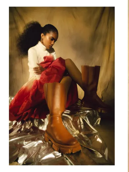 A creative composition from the 'ANAINA' series, with a large boot in the foreground. This unusual perspective adds depth and a touch of surrealism to the fashion portrait.