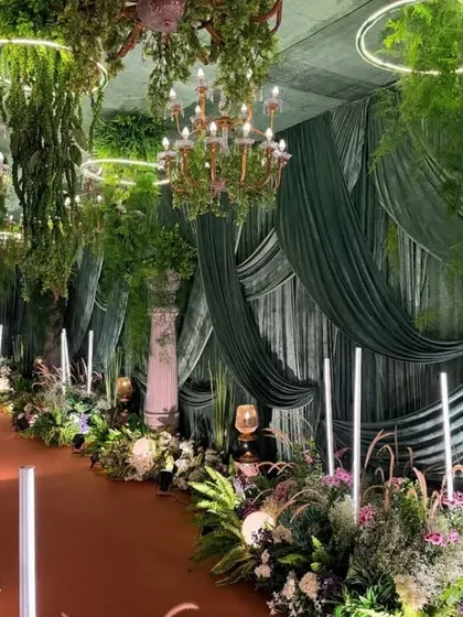 Imagine a sangeet night in an enchanted forest. This design uses deep green velvet drapes, dramatic chandeliers, and lush greenery to create a sophisticated and magical atmosphere perfect for a night of celebration.