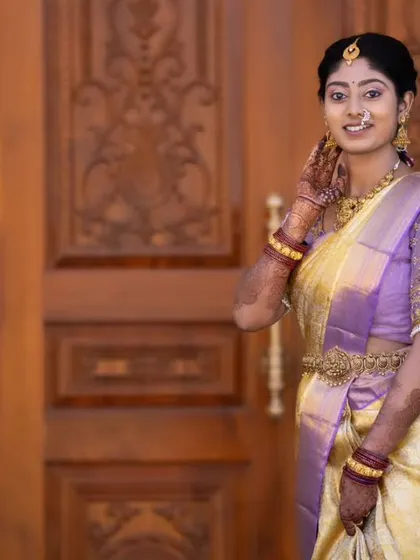 A candid moment against a traditional carved wooden door. Her makeup is soft and natural, letting her beautiful smile and the elegance of her saree take center stage.