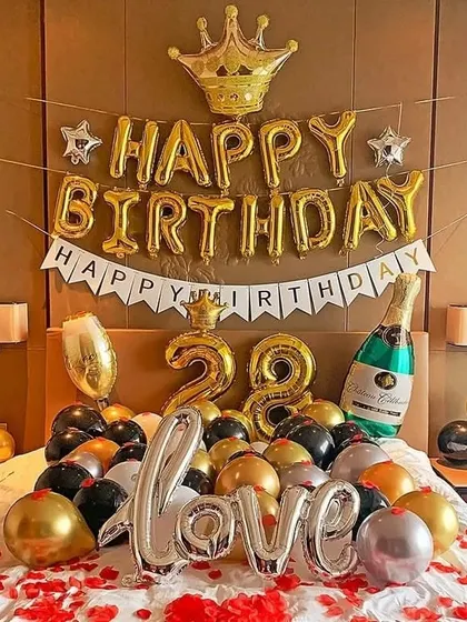 A luxurious birthday bed decoration with gold, black, and silver balloons, a crown foil balloon, and "Love" letter balloons.