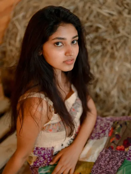 A soft and natural portrait of actress Rachana Inder. The rustic setting with hay bales provides a warm and earthy backdrop, creating a gentle and authentic feel.