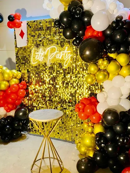 This decoration was designed for a Diwali card party, incorporating playing card motifs into the decor. The gold sequin wall is accented with balloon garlands in red, black, white, and gold to match the casino theme.