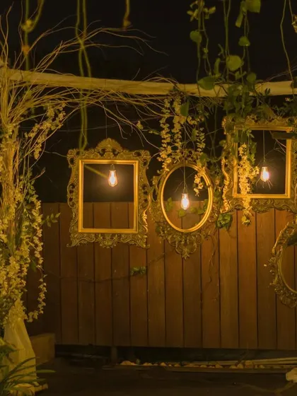 A rustic photo booth corner at night, featuring vintage frames, bare bulbs, and climbing vines for a charming, whimsical feel.