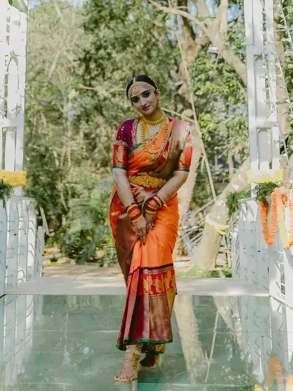 A full portrait of the bride on a bridge, showcasing her entire orange and purple Kanjeevaram wedding ensemble.