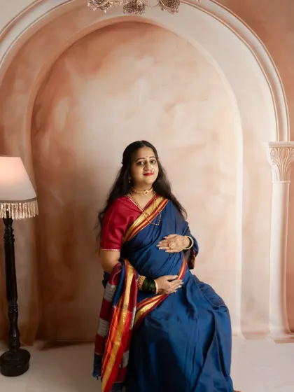 A beautiful portrait of a mother-to-be in a traditional blue saree, seated against a classic archway backdrop.