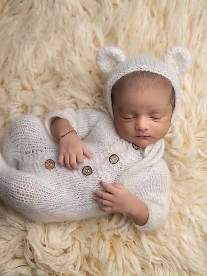 A side pose of the baby in the teddy bear outfit, sleeping on a soft fur rug. This highlights their tiny profile and curled-up posture.