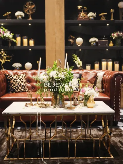 A luxurious lounge setting with a brown leather Chesterfield sofa and a backdrop of shelves filled with candles and curios.