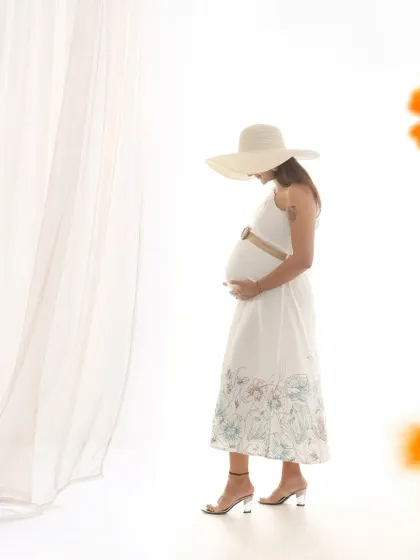 A stylish and artistic solo maternity portrait. The mom-to-be wears a wide-brimmed hat, creating a chic and thoughtful silhouette against a bright, clean background.