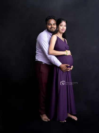 A classic full-length studio portrait of a couple against a solid black background. This timeless setup puts all the focus on the parents-to-be.