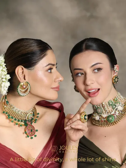 A little bit of divinity, a whole lot of shine. Two models showcase complementary bridal looks, one with a layered green necklace and the other with a pearl and polki choker.