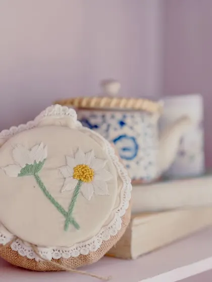 A shelf styled with charming, handcrafted props like embroidered daisies and a vintage teapot.