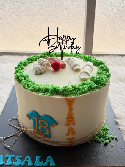 A cricket-themed cake for a Virat Kohli fan. The design features a pitch, a jersey with his number, and other cricket equipment.