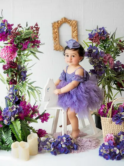 A little princess on her white rocking horse. The vibrant purple and pink flowers create a stunning, colorful backdrop for this milestone portrait.