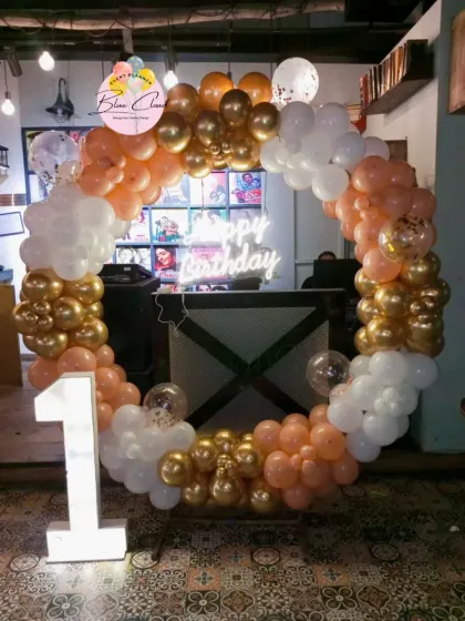 A stylish balloon ring in peach, white, and gold for a first birthday, complete with a marquee number.