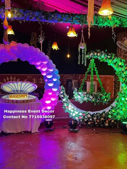A vibrant naming ceremony setup with a mix of traditional and modern elements. It includes a green floral moon-gate with a hanging cradle, a balloon arch, and colorful lighting to brighten up the venue.