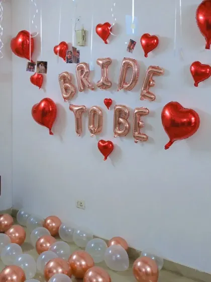 A simple and sweet 'Bride to be' wall decoration using rose gold foil letters, red heart balloons, and balloons scattered on the floor.