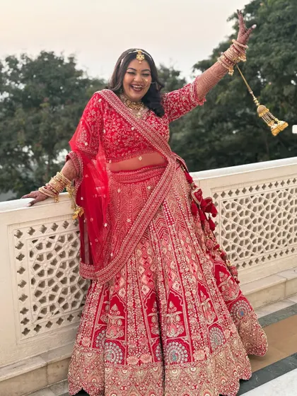 A moment of pure bridal bliss. The bride's vibrant red lehenga and joyful expression are the highlights, supported by a makeup look that enhances her natural beauty without overpowering it.
