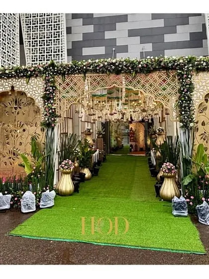 A grand, opulent entrance for a large-scale wedding. The design features intricate golden panels, elephant motifs, and a lush green carpet, creating a royal and unforgettable first impression.
