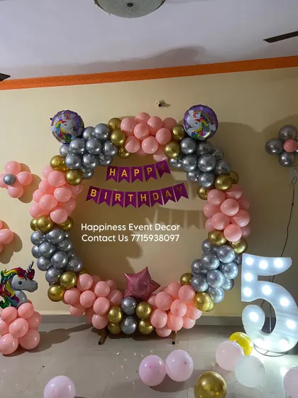 A unicorn-themed 5th birthday party decor. This home setup features a balloon ring in pink, silver, and gold, along with a large light-up number '5' and unicorn-themed foil balloons.