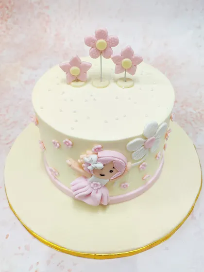 We design pure sweetness for a baby girl's first birthday with this girly flower cake. A charming fondant girl floats among pink and white flowers on a simple, elegant cake, creating a whimsical and delicate centerpiece.