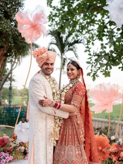 A classic wedding portrait with the couple looking at the camera, surrounded by the beautiful orange and pink decor of their outdoor wedding.