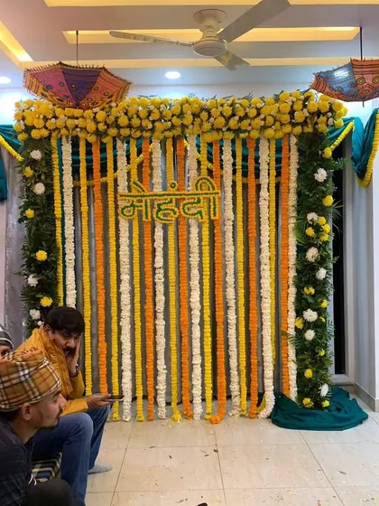This is a classic Mehndi backdrop we set up in a client's home. It features strings of fresh yellow, white, and orange marigolds with a "Mehndi" sign, perfect for traditional pre-wedding functions in a compact space.