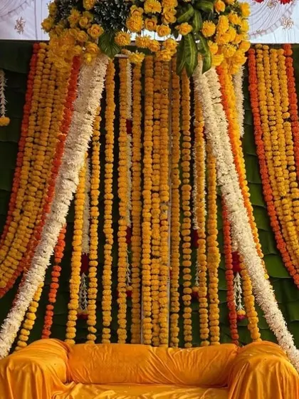 A sofa decorated for a Haldi ceremony with a yellow cover and a canopy of dense marigold and jasmine flower strings.