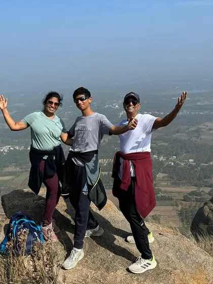 A family of three celebrating with arms raised at a scenic viewpoint. We love seeing families experience the joy of trekking together.