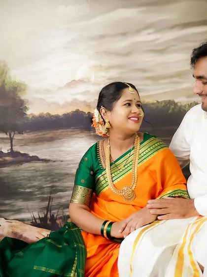 A traditional couple's portrait celebrating their cultural heritage. Dressed in beautiful ethnic attire, they share a sweet moment against a painted landscape backdrop.