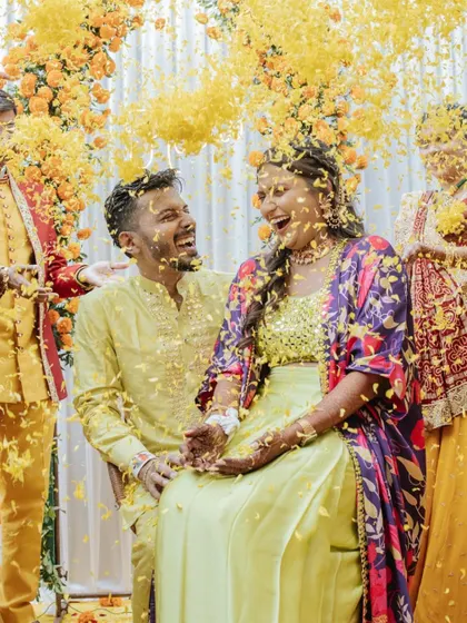 A joyous moment as Shreya and Harsh are showered with marigold petals during their Haldi ceremony, their faces lit up with laughter.
