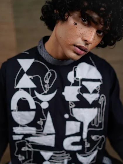 A close-up portrait focusing on the artistic details of the garment and the unique makeup. The abstract patterns on the clothing are mirrored in the small hash symbol drawn on the model's face.
