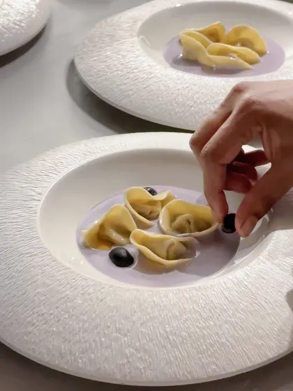 A chef carefully plating tortellini in a lavender-colored sauce. This dish was part of a menu where each course was designed to reflect the balance and form of the art at Galerie Isa.