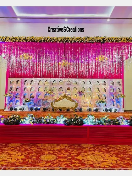 A glamorous stage with a silver tinsel backdrop and a 'jharokha' panel. The bright pink draping and floral arrangements create a fun and celebratory atmosphere.