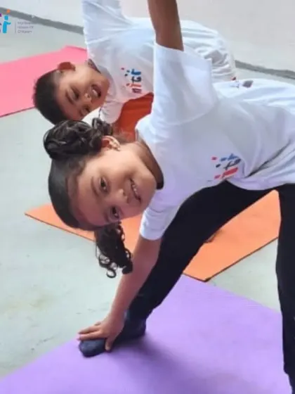 Two children smile as they practice a standing side-stretch. We make yoga fun and accessible for our young learners.