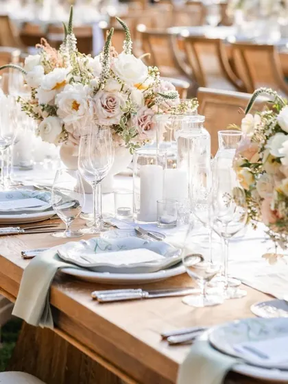 A bright, sunlit shot of a tablescape featuring soft pastel florals in white urns. The elegant glassware and custom plates complete this timeless and romantic look for a wedding luncheon.