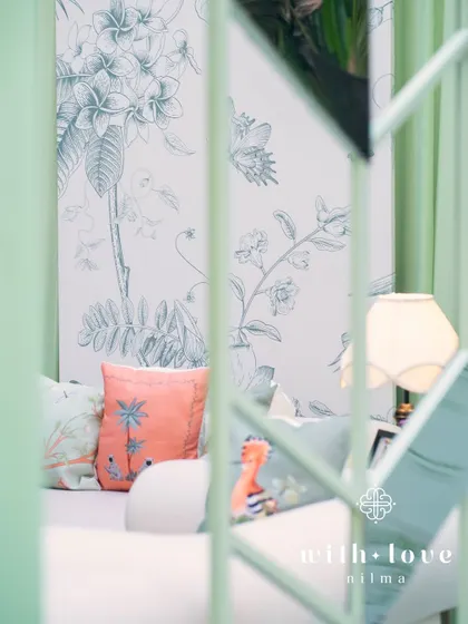 A peek through the sage green structure of 'The Conservatory', revealing the custom botanical wallpaper and colorful accent pillows inside.