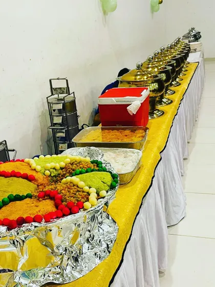 A full buffet spread for an apartment party in Hennur. This setup includes a colorful sweet dish, multiple main courses in chafing dishes, and stacked tiffins for any takeaway needs.