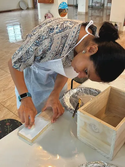 A participant carefully sanding her wooden box to create a distressed effect. This process reveals layers of color and texture.