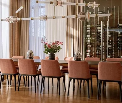 This view shows the Luna Kaleido fixture spanning the length of a long dining table, with a wine cellar in the background. It's a perfect example of lighting designed for luxurious entertaining.