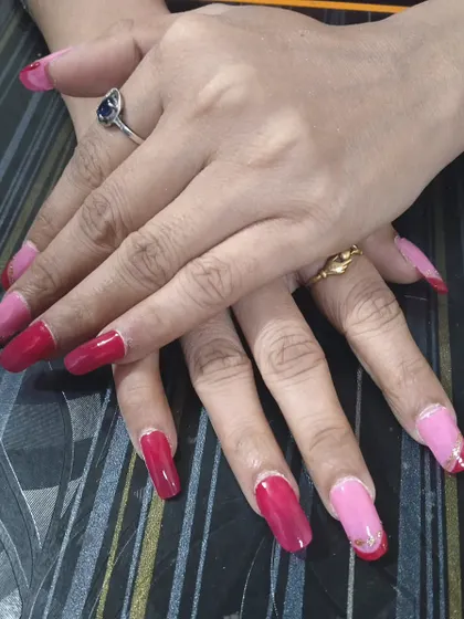 A client showing off her new set of custom press-on nails. This design features a mix of pink and red with a delicate silver line accent for a stylish, mismatched look.