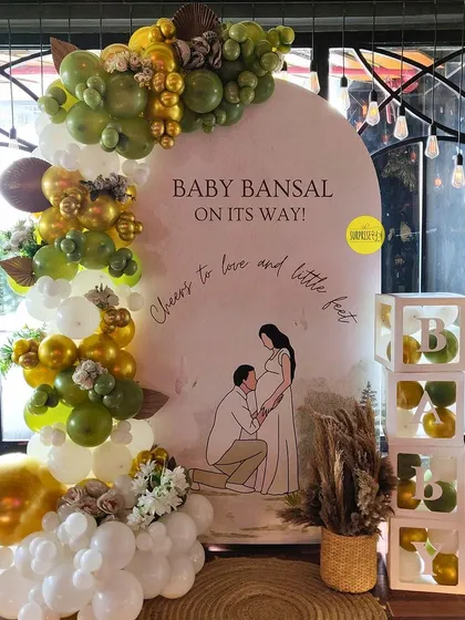 This personalized baby shower backdrop features a sweet illustration of the parents-to-be. The olive green and white balloon arch with pampas details adds a touch of boho elegance.