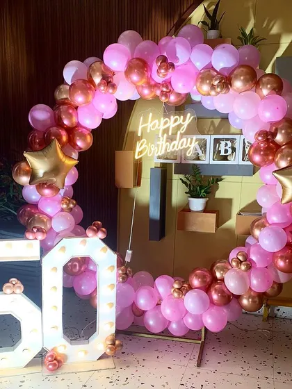 A vibrant 50th birthday celebration with a circular balloon frame in shades of pink and rose gold. Large marquee numbers and a "Happy Birthday" neon sign make it a festive photo corner.