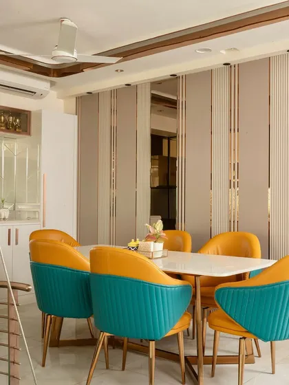 The dining area is a feast for the eyes, with bold turquoise and yellow chairs, a marble-top table, and a stylish paneled wall with mirrored accents.