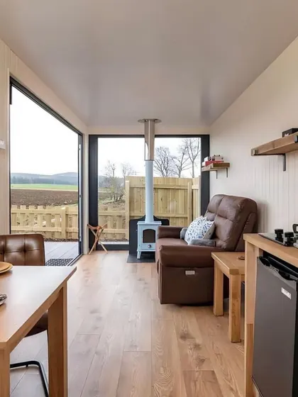 This living area in a container home is designed to be cozy and functional, with a small dining table and a comfortable armchair overlooking the outdoors.