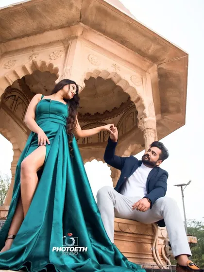 A dramatic and stylish pre-wedding shot against a stone gazebo. The bride's high-slit gown and the couple's pose create a confident and fashionable look.