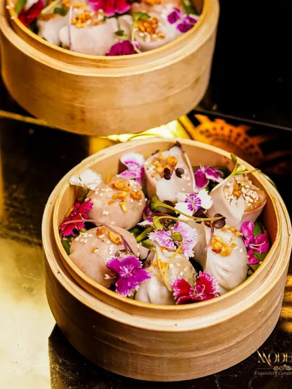 A close-up of our artfully crafted dim sum, garnished with edible flowers. Each piece is a delicate parcel of flavor, steamed to perfection and presented beautifully in traditional bamboo baskets, making them a highlight of our Pan-Asian menu.